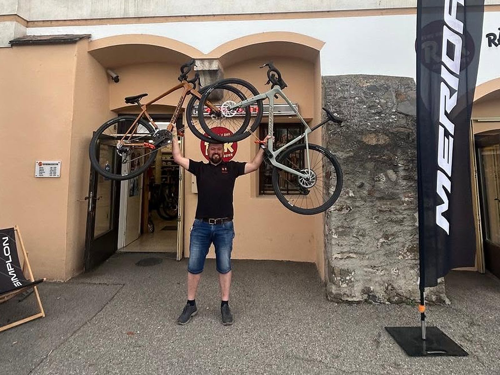 Andreas Geyer vor dem Eingang von Rund ums Rad, zwei Fahrräder über dem Kopf