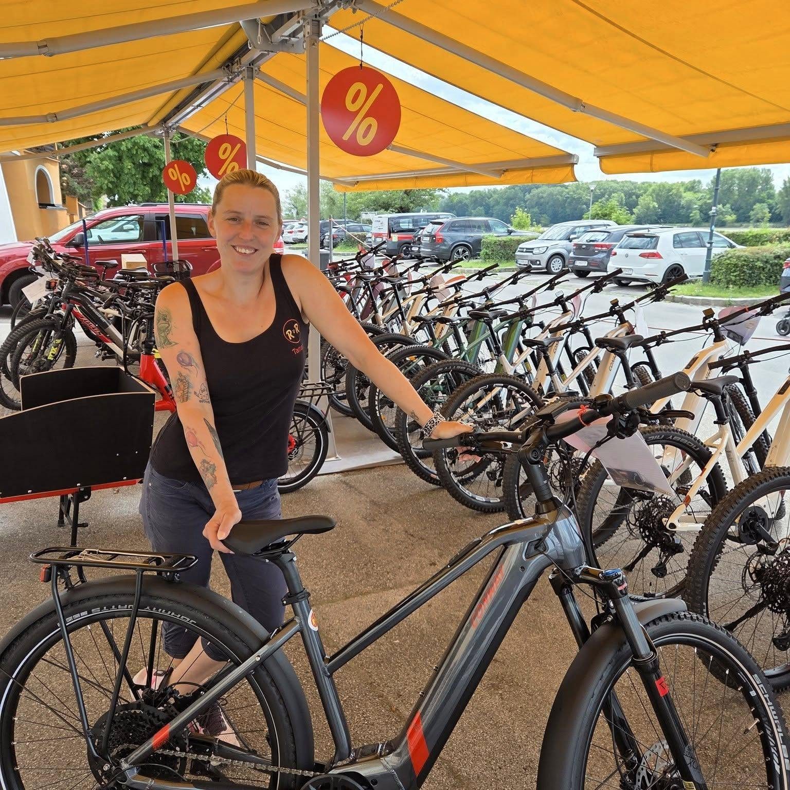 Tamara zeigt ein E-Bike unter der Markise vor dem Geschäft